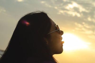 Close-up of woman wearing sunglasses against sky at sunset