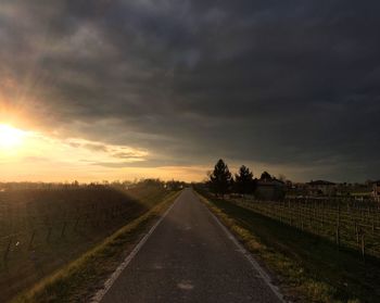 Road amidst field against sky during sunset