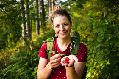 Portrait of smiling young woman holding apple against trees in forest