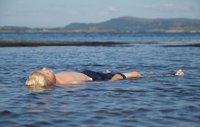 Boy floating in sea against sky