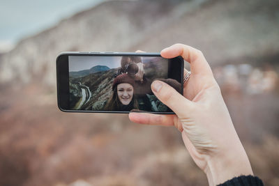 Cropped hand of woman taking selfie while man photographing with camera