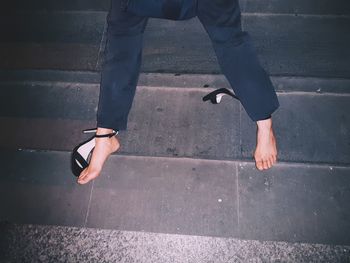 Low section of woman with broken high heels sitting on staircase