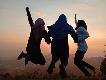 Rear view of friends walking on land against sky during sunset