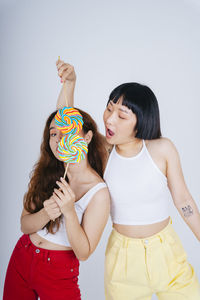 Lesbian couple holding lollipop against white background