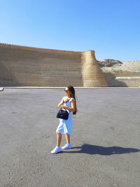 Full length of woman standing on street against clear sky