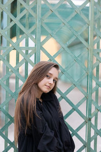 Portrait of young woman standing by metal grate outdoors