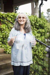 Smiling senior woman standing with water pitcher and glass in back yard