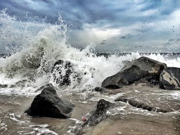 Waves splashing on rocks against cloudy sky