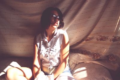 Sunlight falling on young woman sitting on bed at home