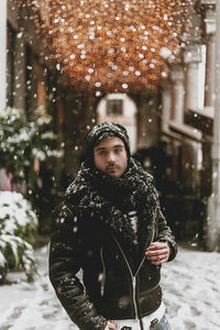 Portrait of man standing in snow against illuminated lighting equipment outdoors