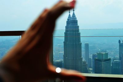 Optical illusion of cropped hand holding petronas towers in city