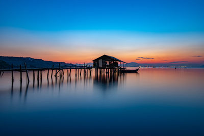 Wooden posts in lake against sky during sunset