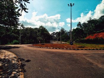 Empty road by trees against sky