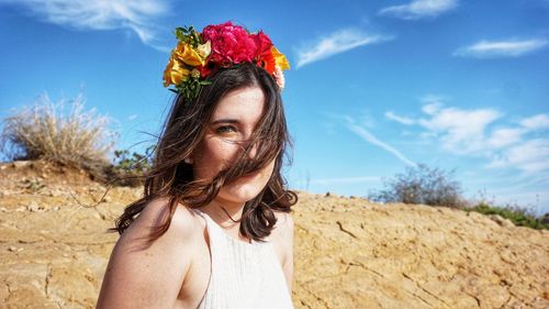 Portrait of young woman with pink flowers against sky