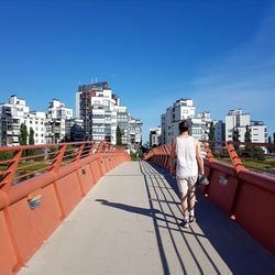 Rear view of man walking on bridge in city