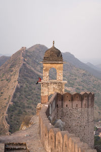 Woman sitting in arch of old tower against mountain ridge and walls while visiting amer fort viewpoint in jaipur, india