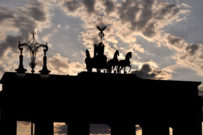 Low angle view of silhouette brandenburg gate against cloudy sky during sunset