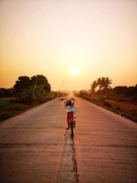 Rear view of man riding bicycle on road against sky during sunset