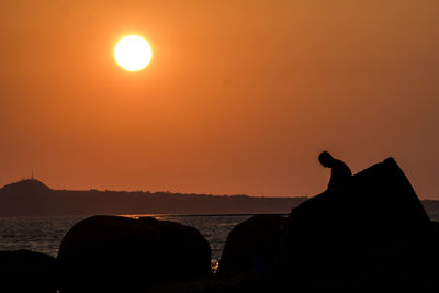 Silhouette horse by sea against orange sky