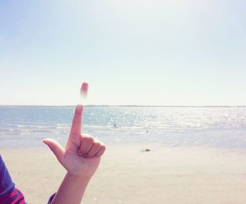 Optical illusion of cropped hand pointing at beach against sky