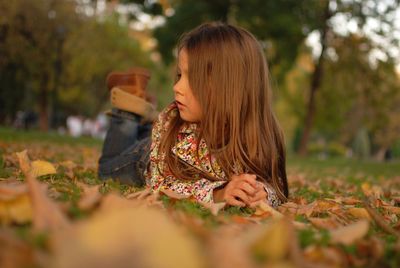 Thoughtful girl resting on field in park during autumn