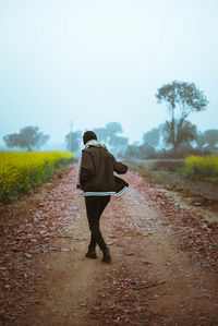 Rear view of man walking on footpath amidst field