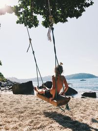 People sitting on swing at beach against sky