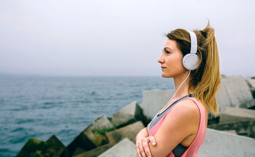 Woman listening music at beach against sky