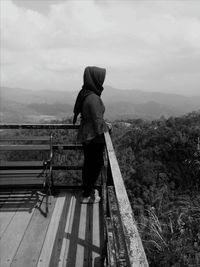 Rear view of man standing on railing against mountain