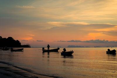 Silhouette fishing boats in sea against sky during sunset