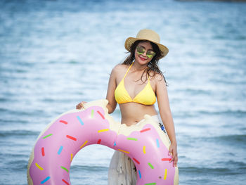 Portrait of woman with inflatable ring standing against sea