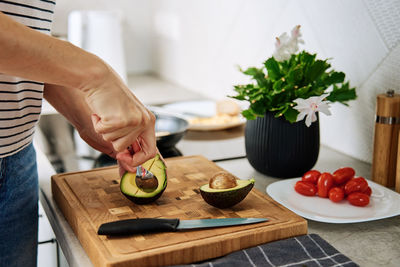 Woman cutting avocado on cutting board to prepare breakfast