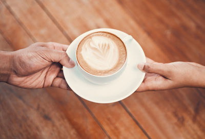 Cropped image of hand holding coffee on table