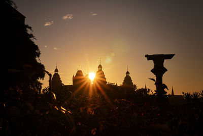 Silhouette of temple against building during sunset