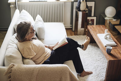 High angle view of woman with disability reading book while sitting on sofa at home