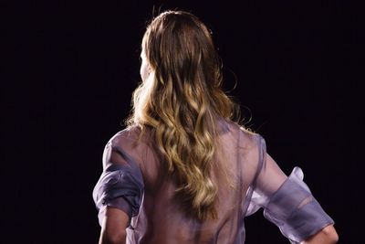 Rear view of young woman standing against black background