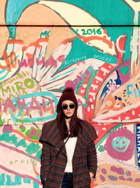Portrait of young woman standing against graffiti wall