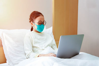Midsection of man using mobile phone while sitting on bed at home
