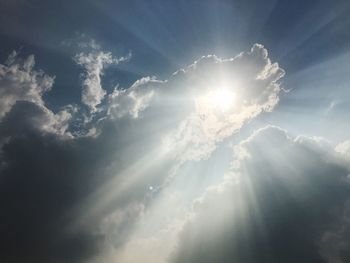 Low angle view of sunbeams streaming from clouds