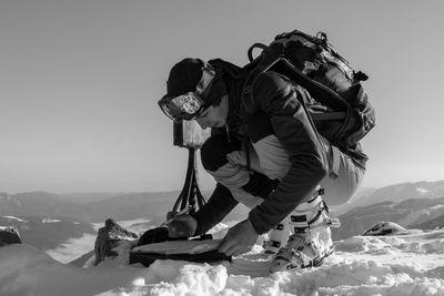 Male hiker reading map at snow covered mountain against sky