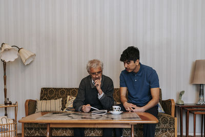 Senior man discussing with male caregiver sitting on sofa at home