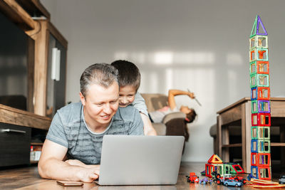 Dad works at home on a laptop and plays with his son at the same time. the child hugs dad