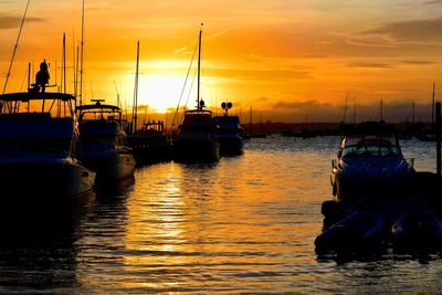 Sailboats moored in sea against sky during sunset