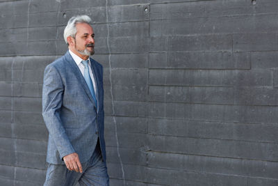 Mature businessman walking by gray wall