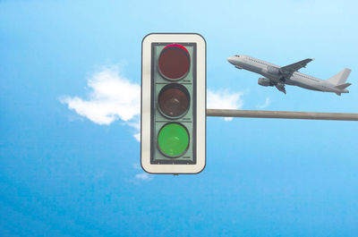 Low angle view of road signal and airplane against blue sky