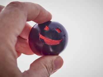 Close-up of hand holding black tomato over white background