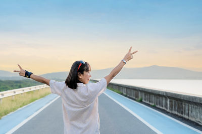 Back view of a female tourist rising hands up in the air. woman traveler standing on street of dam