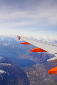 Cropped image of airplane flying over mountains against cloudy sky