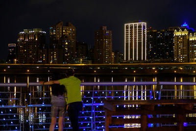 Rear view of man looking at illuminated modern buildings in city at night