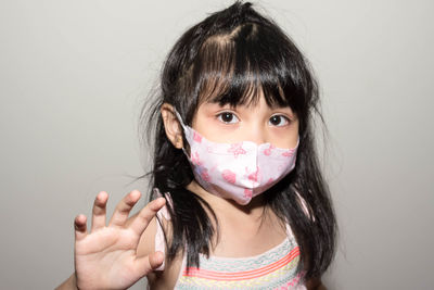 Close-up portrait of girl waving while wearing mask against white background